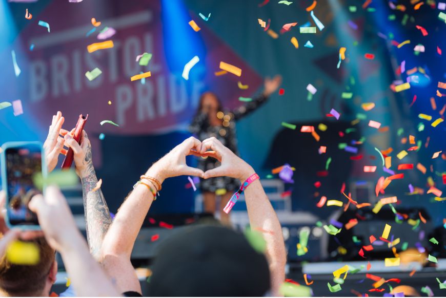 someone doing a heart with their hands in a crowd, rainbow confetti falling on them